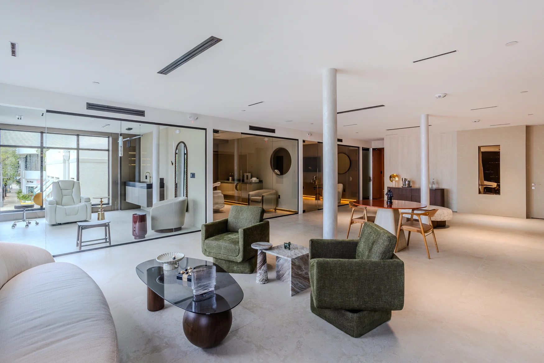 Bright lounge with a cream sofa, green armchairs and glass-fronted rooms with reclining chairs.