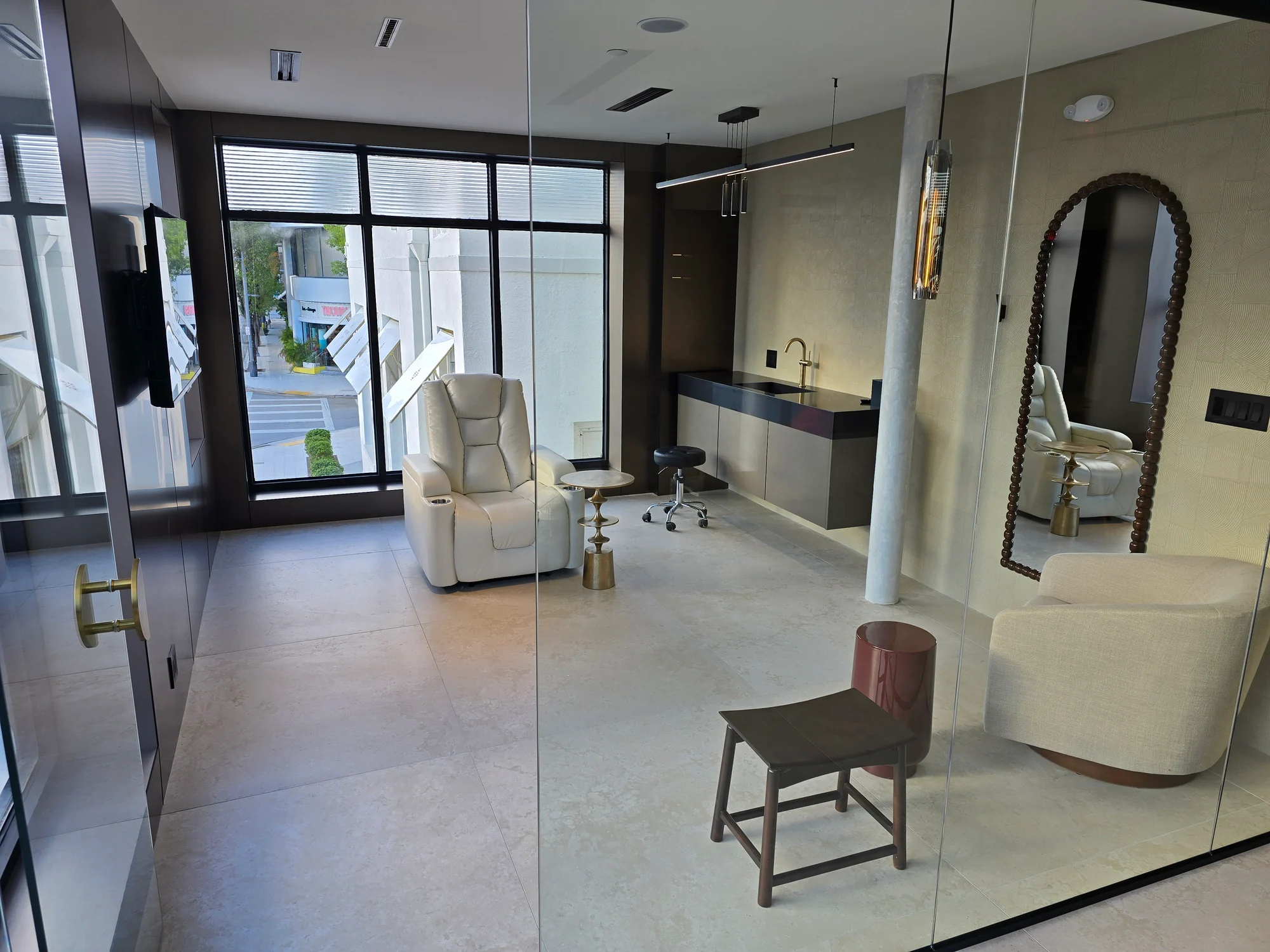 A glass-fronted room with white reclining chairs, a sink and a large window.